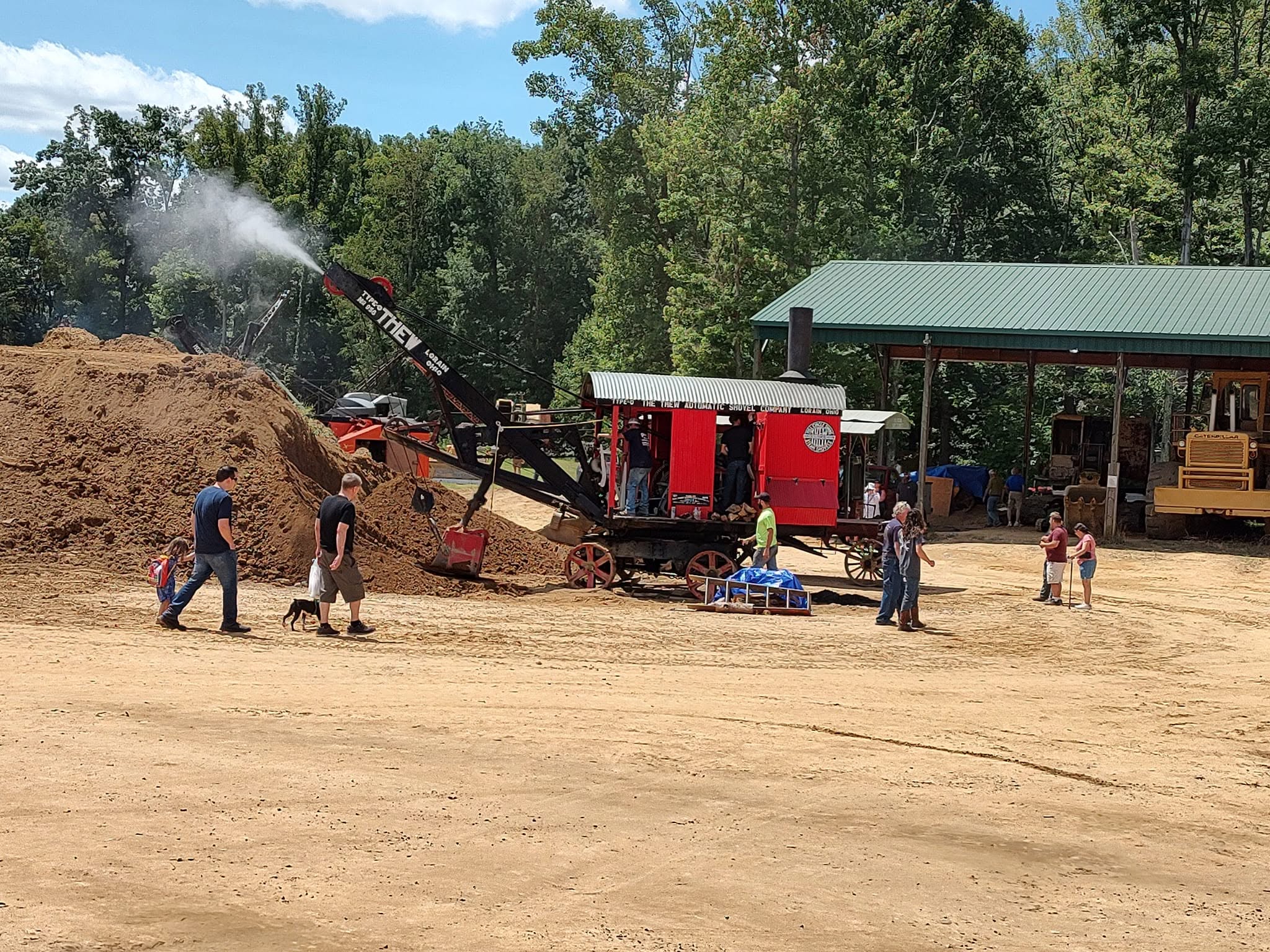 Red steam-powered traction engine with a blowing steam jet next to a large dirt pile