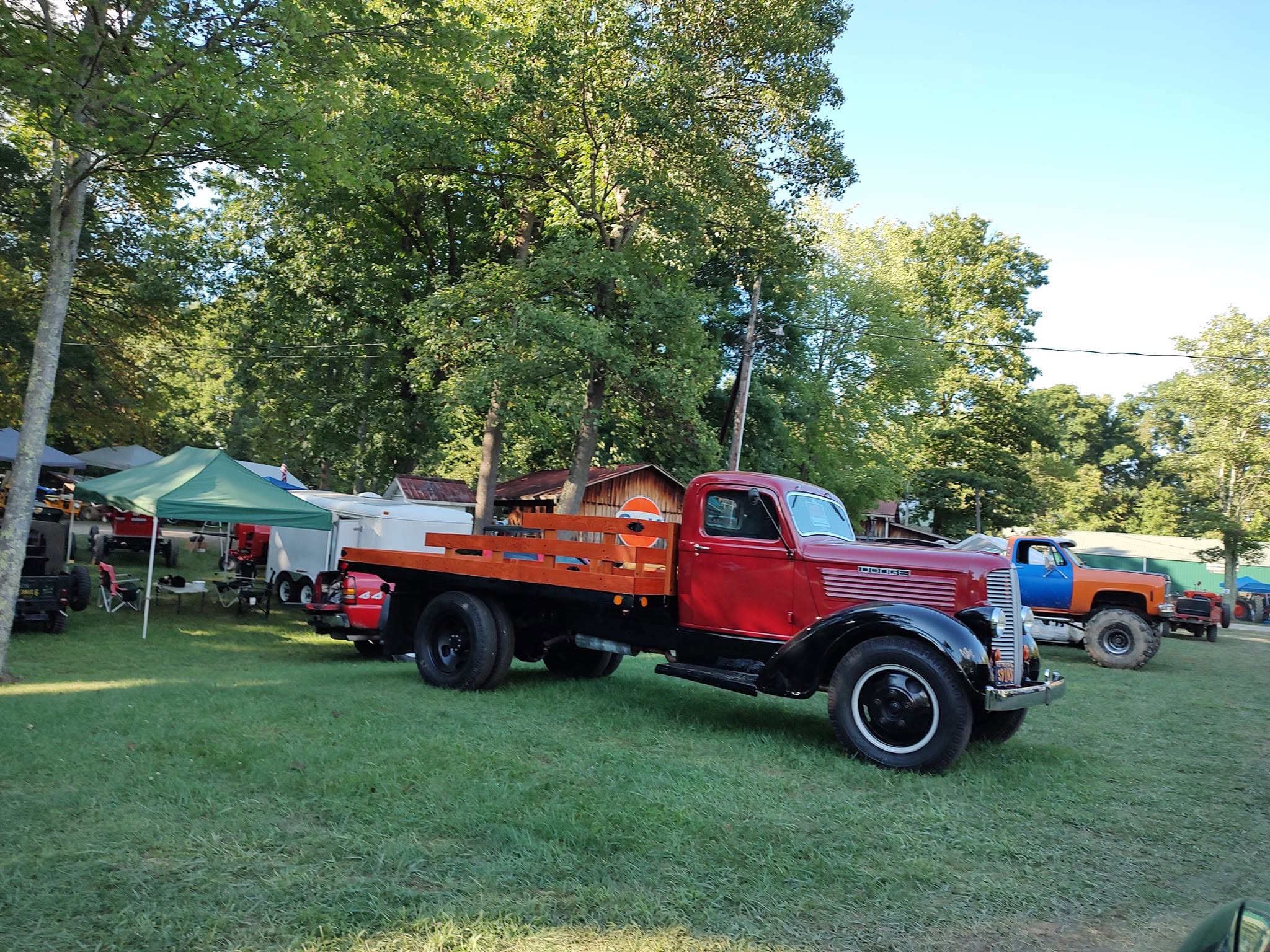 Classic 1940s red flatbed stake truck parked on grass beside vendor tents