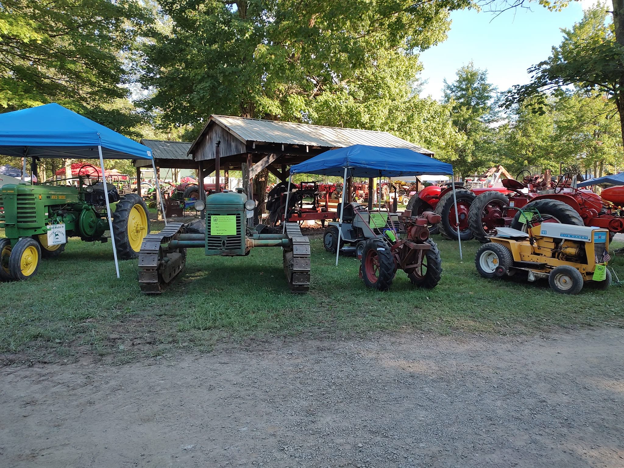 Green John Deere crawler, Oliver tractor, and yellow lawn tractor displayed under blue canopy tents
