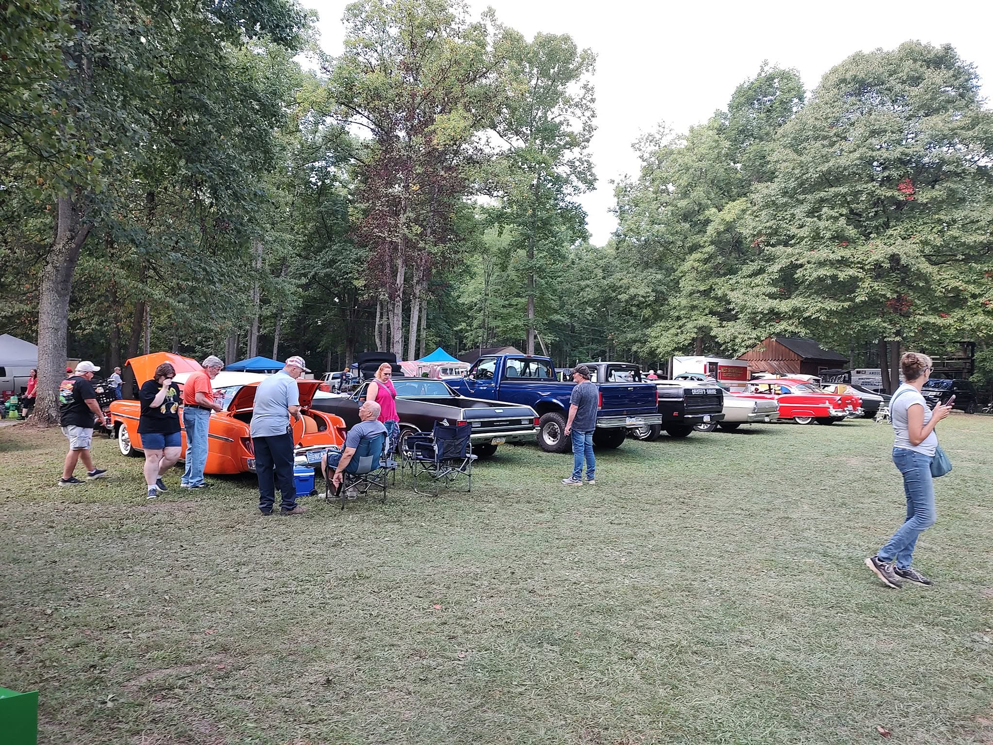 Classic car show lineup with muscle cars and old pickups on the grass in evening light